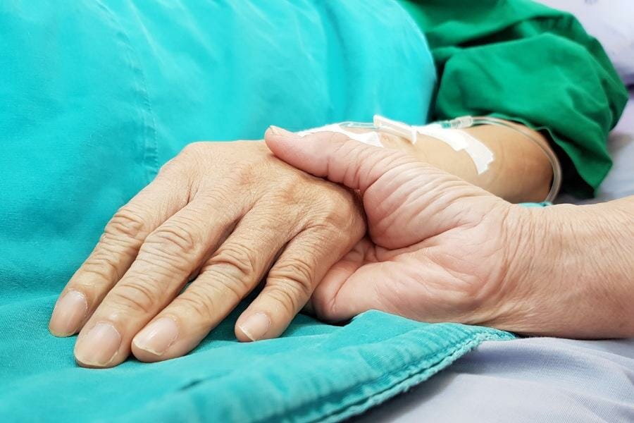 A palliative nurse holding a elderly patients hand.