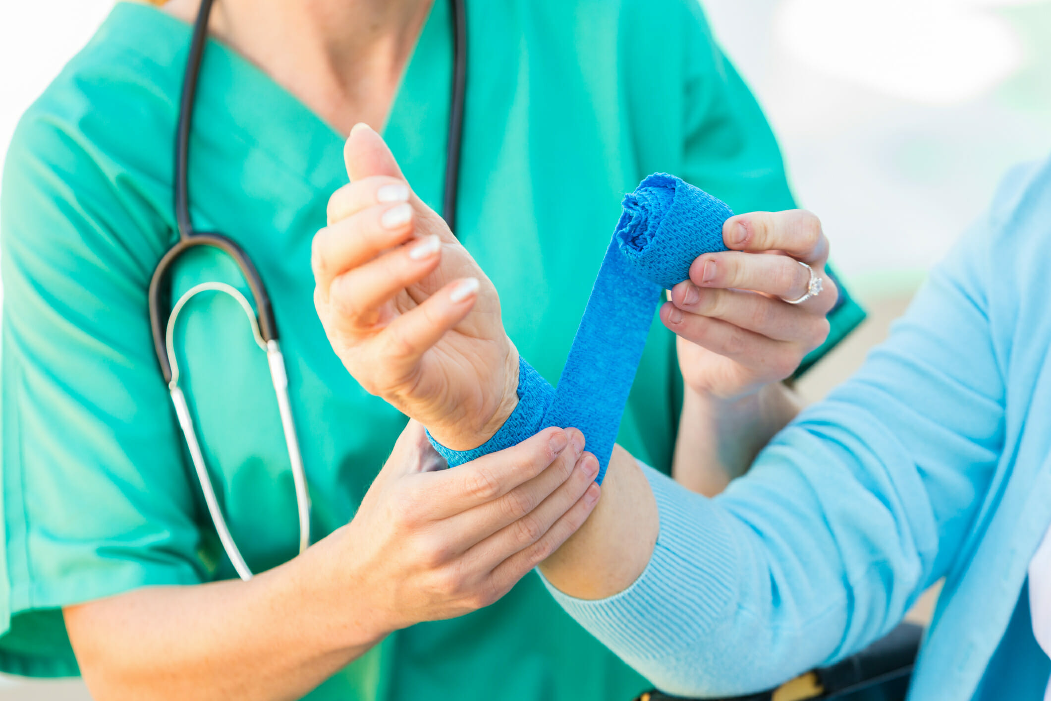 Nurse wrapping bandage on the wrist of injured senior adult