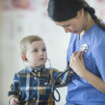 A little boy is using a stethoscope to listen to the nurses heartbeat.