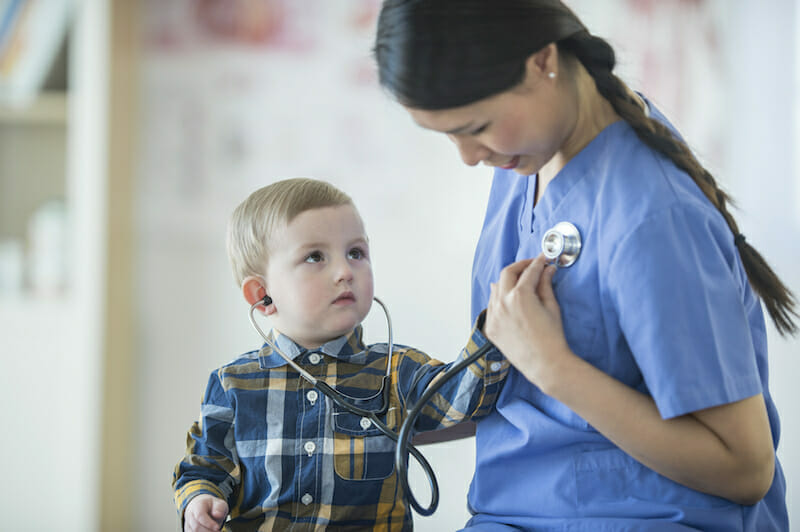 A little boy is using a stethoscope to listen to the nurses heartbeat.