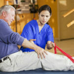 Physical therapist (20s) helping patient (60s) with exercises to help injured knee.