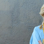 blonde female nurse smiling with blue scrub top on and yellow stethoscope