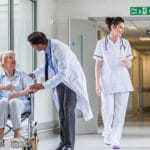 a hallway of a hospital with nurses, a doctor and patient