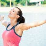 young woman taking a deep breath by a lake