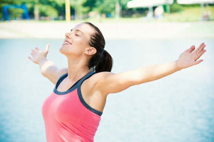 young woman taking a deep breath by a lake