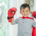 young boy wearing boxing gloves and hooked to a hanging bag via iv