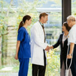 senior couple leaving hospital and saying thank you to doctor and nurse