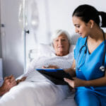 Hospital nurse is helping senior woman create a discharge plan with husband holding woman's hand.
