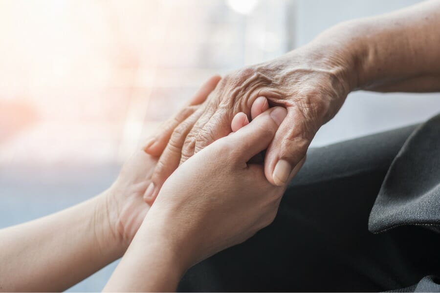 A loved one holding the hand of a senior citizen with Alzheimer's Disease