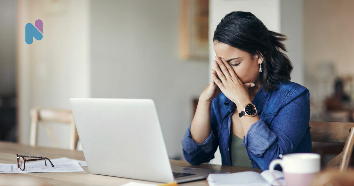 working woman at desk with laptop holding nose and looking like she has burnout