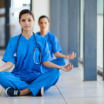 two female nurses in blue scrubs sitting on hospital floor meditating