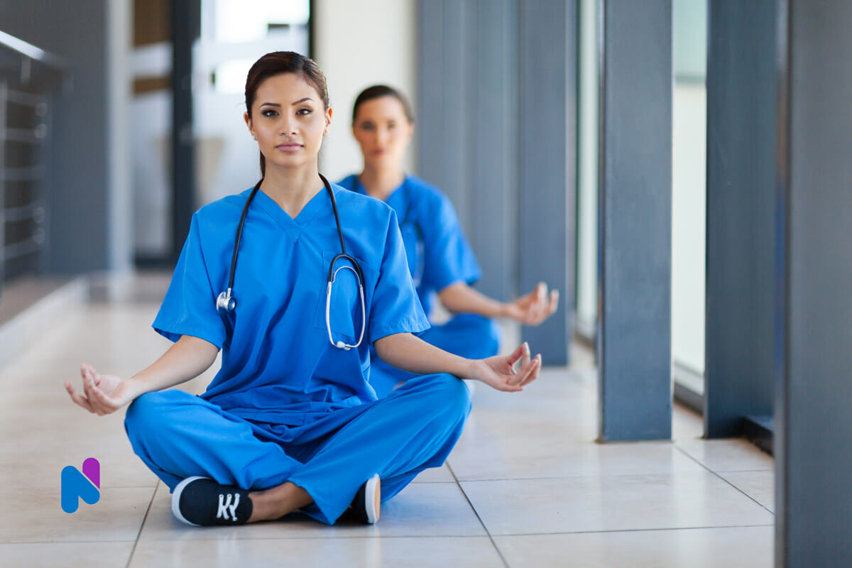 two female nurses in blue scrubs sitting on hospital floor meditating