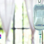 close up of iv bag hanging on pole with windows in background