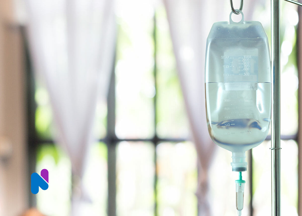 close up of iv bag hanging on pole with windows in background