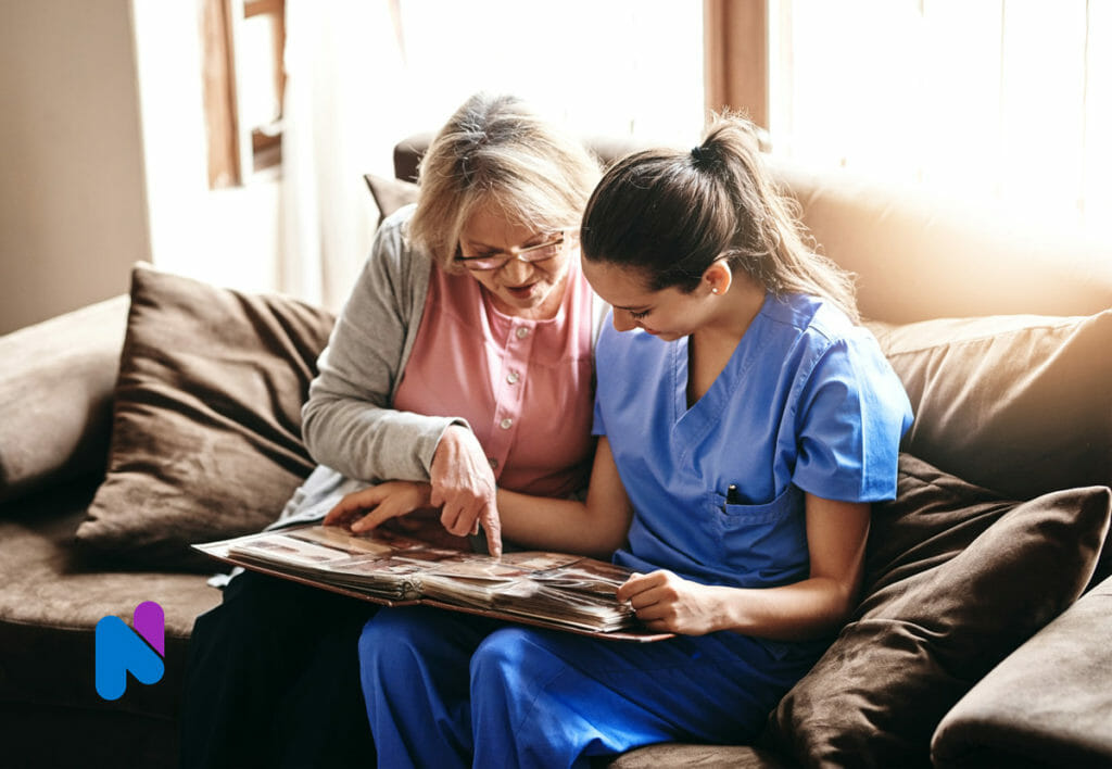 older senior adult with nurse at home looking at photo album memories