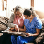 older senior adult with nurse at home looking at photo album memories