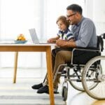 father sitting in rental wheelchair with son in his lap
