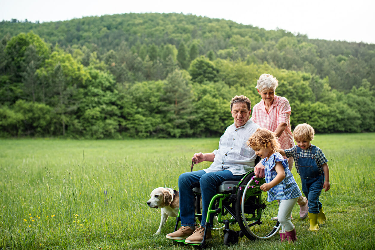 family out for a walk grandfather in wheelchair grandhildren and dog walk along side