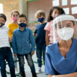 SSchool nurse during the COVID-19 pandemic surrounded by kids wearing facemasks