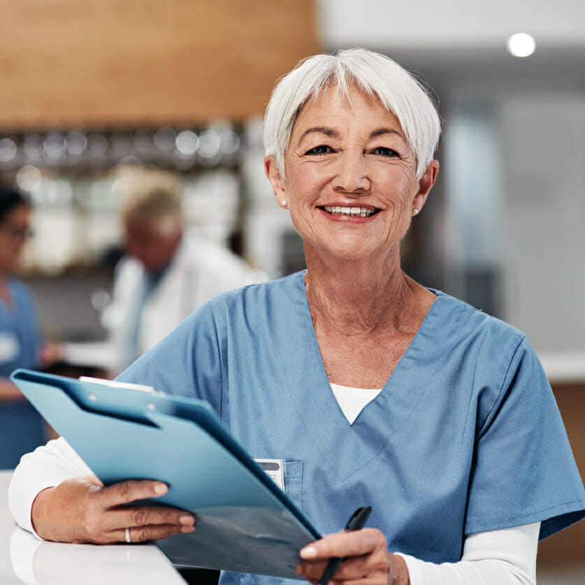 experienced nurse holding file and standing at nurses station