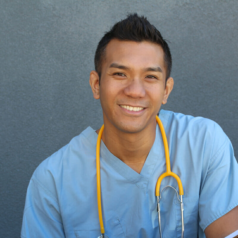 young asian male nurse in blue scrubs with stethoscope and holding clipboard