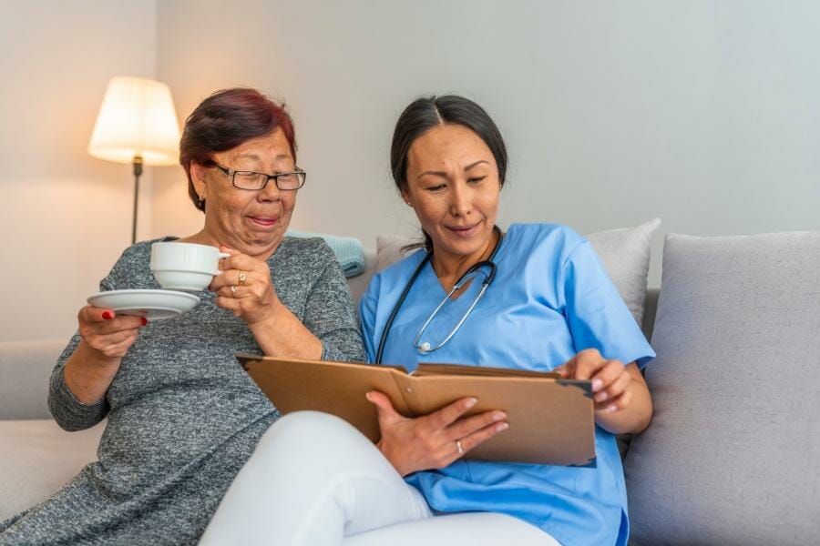 a happy home nurse and her elderly patient on the couch.