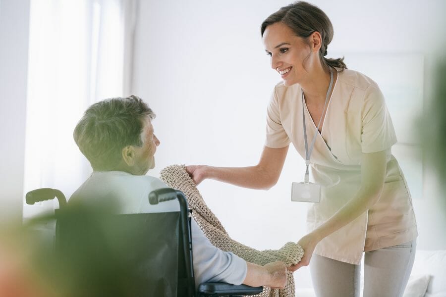 A smiling nurse with an elderly patient in a wheel chair.