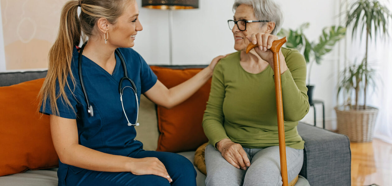 Female nurse in blue scrubs and stethoscope is visiting senior woman at her home