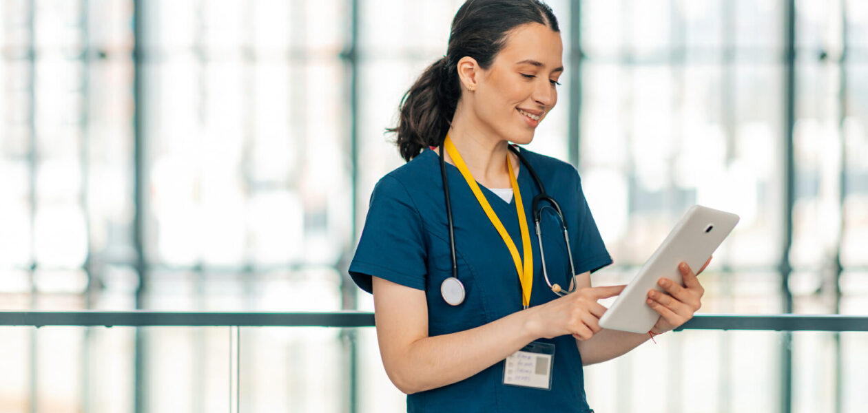 female nursing staff in blue scrubs looking at ipad in medical building