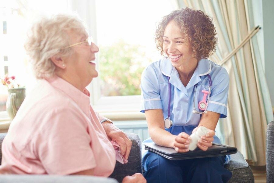 A private nurse laughing with her elderly client.