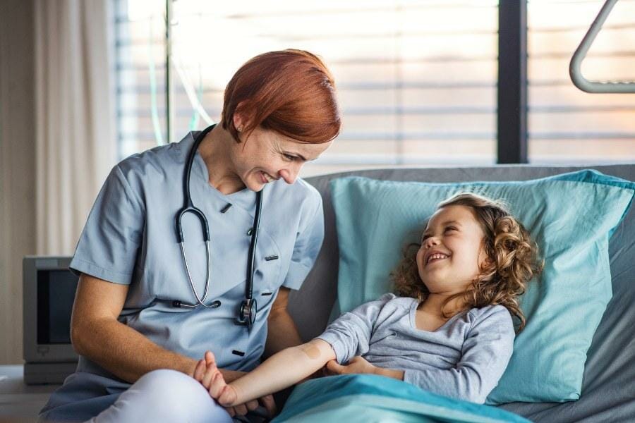 A pediatric nurse laughing with a young patient.