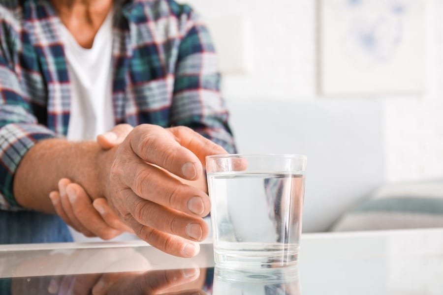 A man with Parkinsons struggling to grab a glass of water